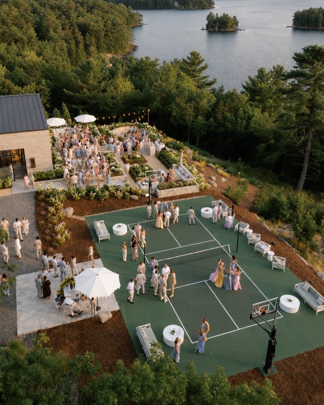 Guests gathered on a lakeside court at dusk, seen from above